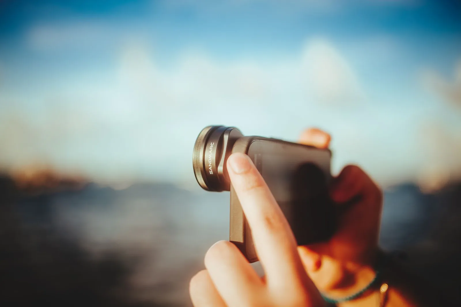 Close-up of hands using a smartphone with a lens attachment to take photos outdoors
