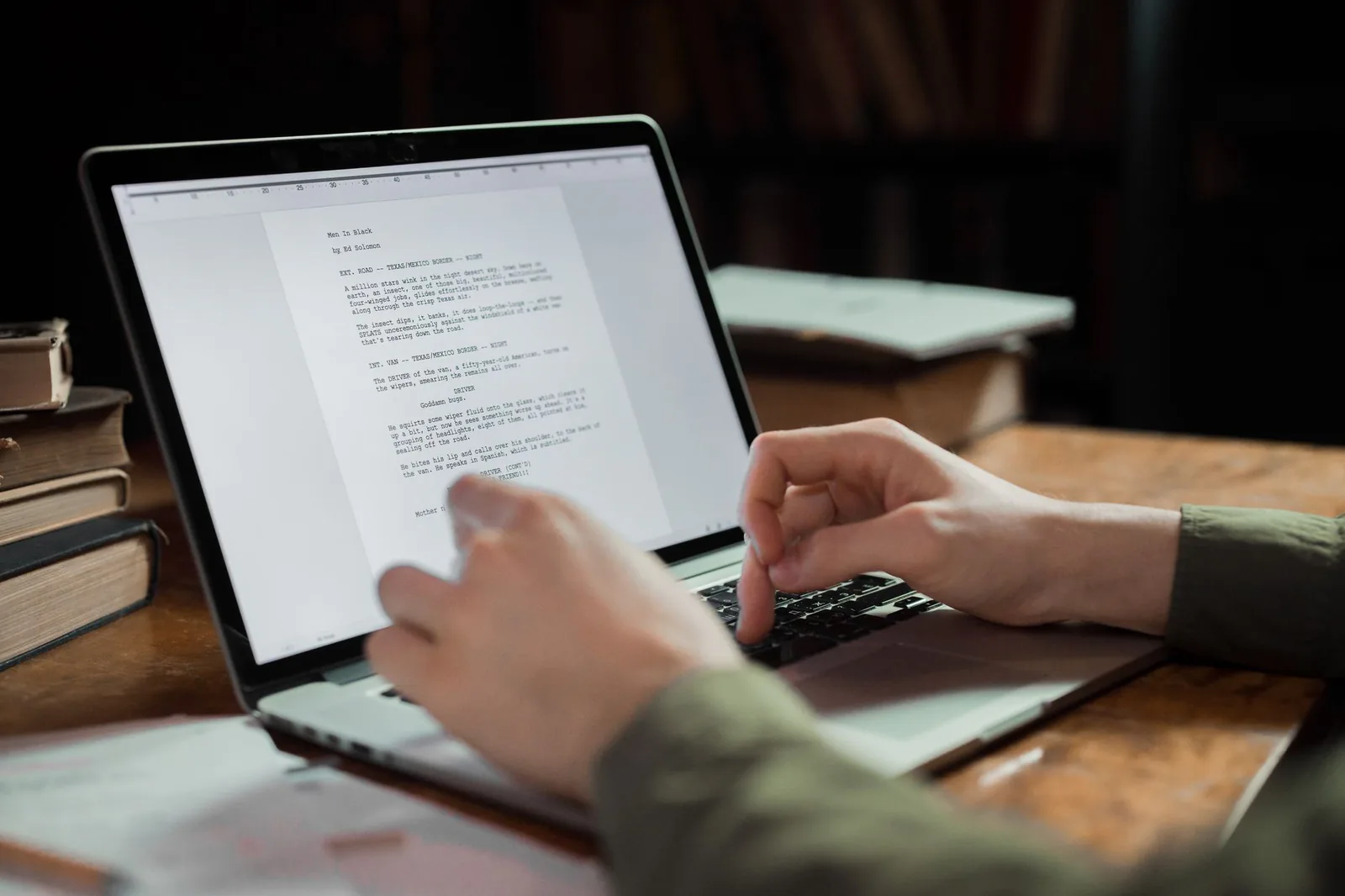 Writer working on manuscript on laptop surrounded by books